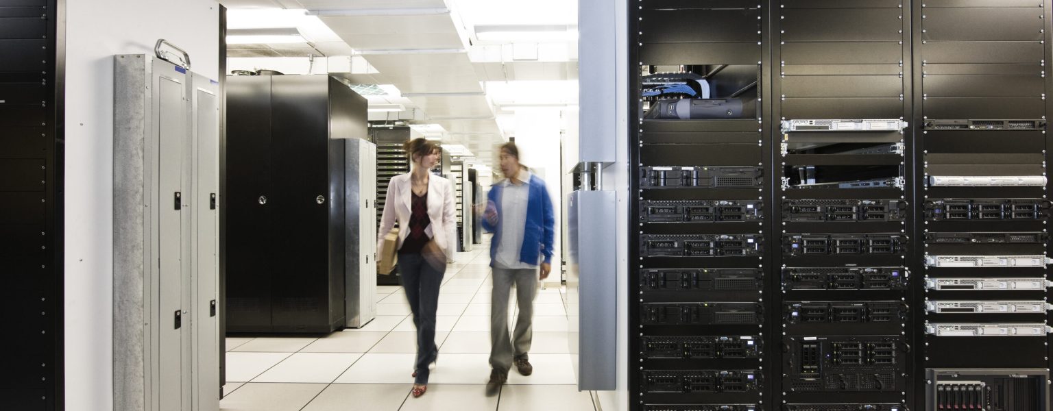 Computer server room racks with technician in background.