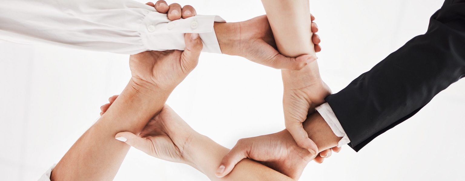 Low angle shot of a group of businesspeople holding one anothers wrists in a circular formation.